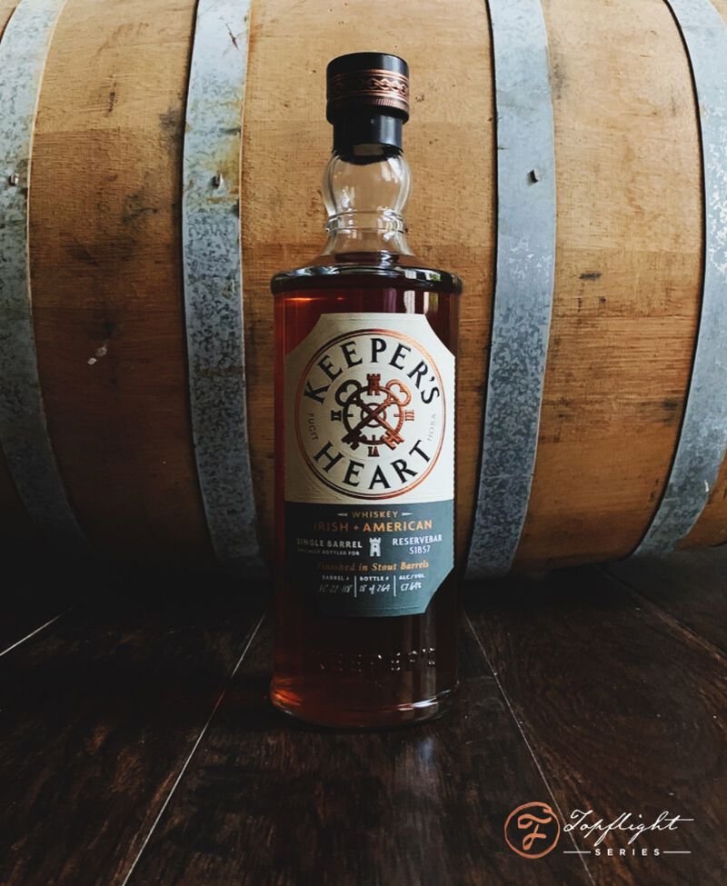 A bottle of Keeper’s Heart Stout Barrel Finished Irish + American Whiskey S1B57 in front of a barrel