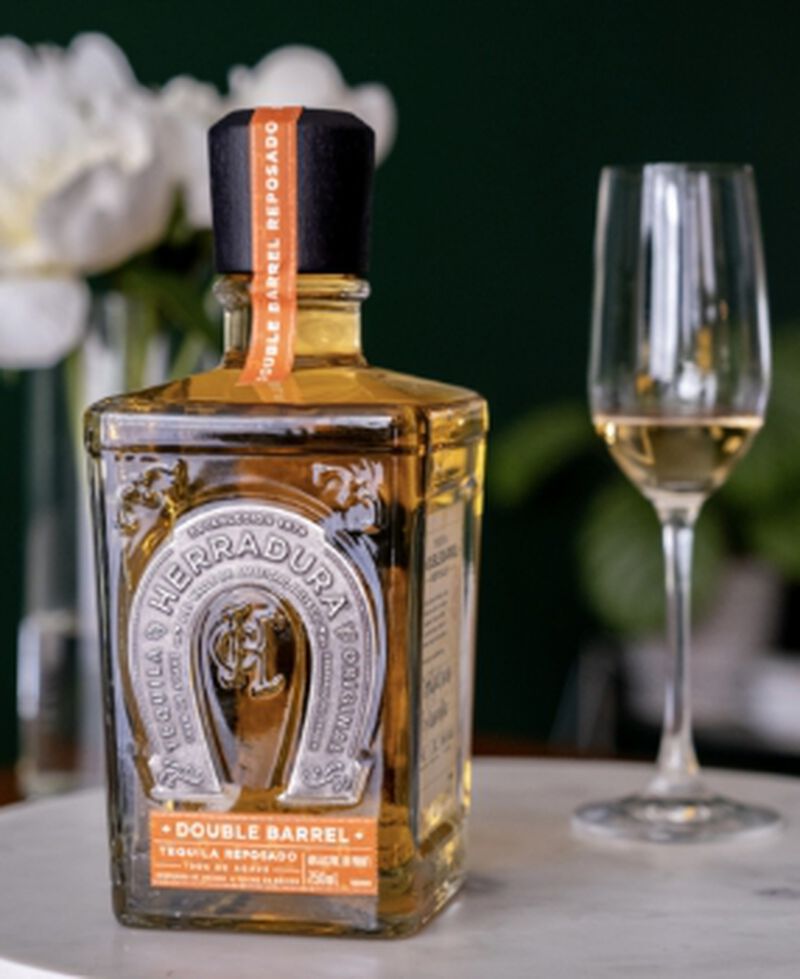 Bottle of Tequila Herradura Double Barrel Reposado S1B58 with a tasting flute and flowers