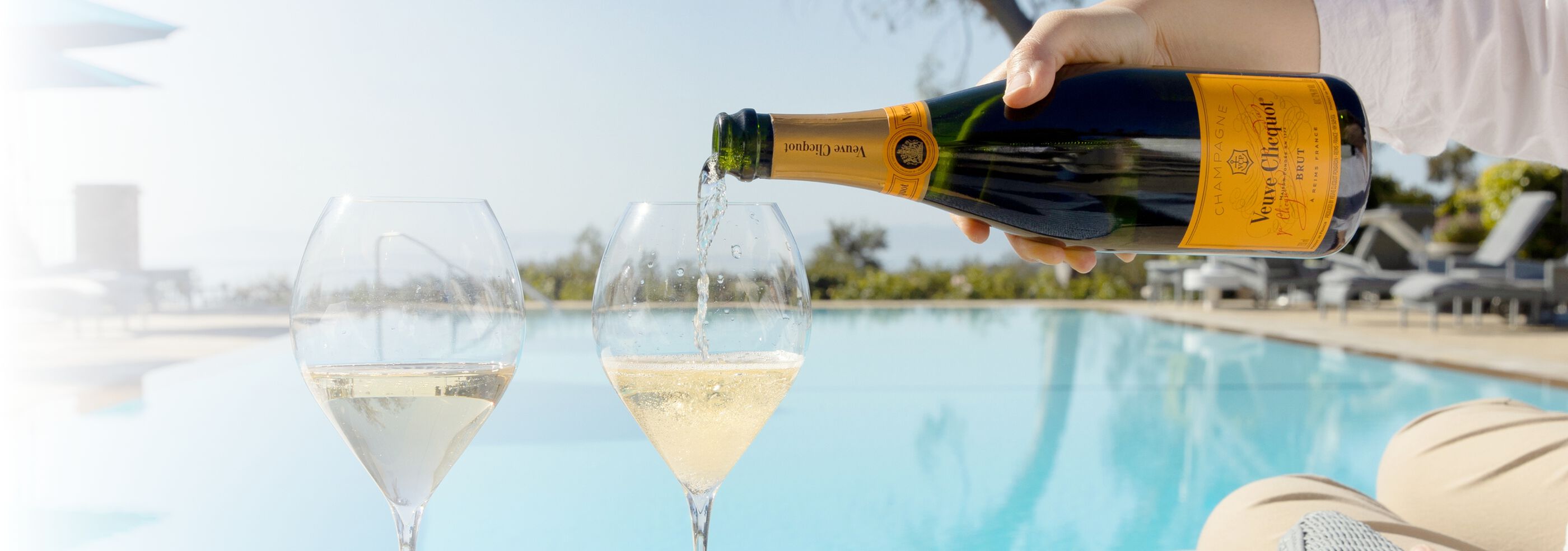 A bottle of Veuve Clicquot being poured into flute glasses poolside