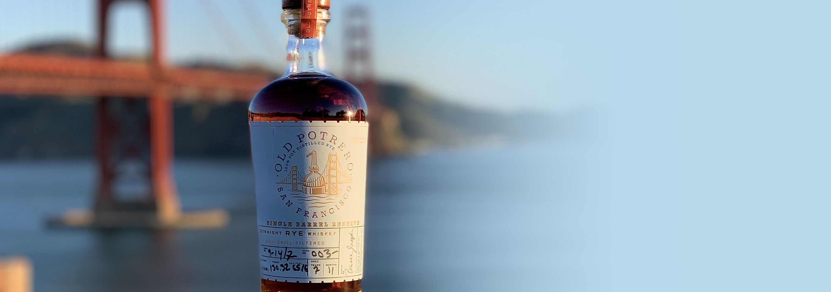 A bottle of Old Potrero Single Barrel Straight Rye Whiskey S1B45 in front of the Golden Gate Bridge