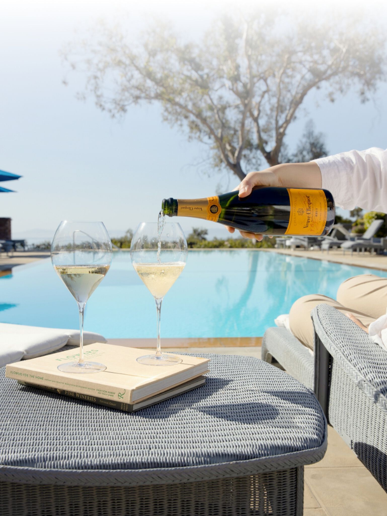 A bottle of Veuve Clicquot being poured into flute glasses poolside